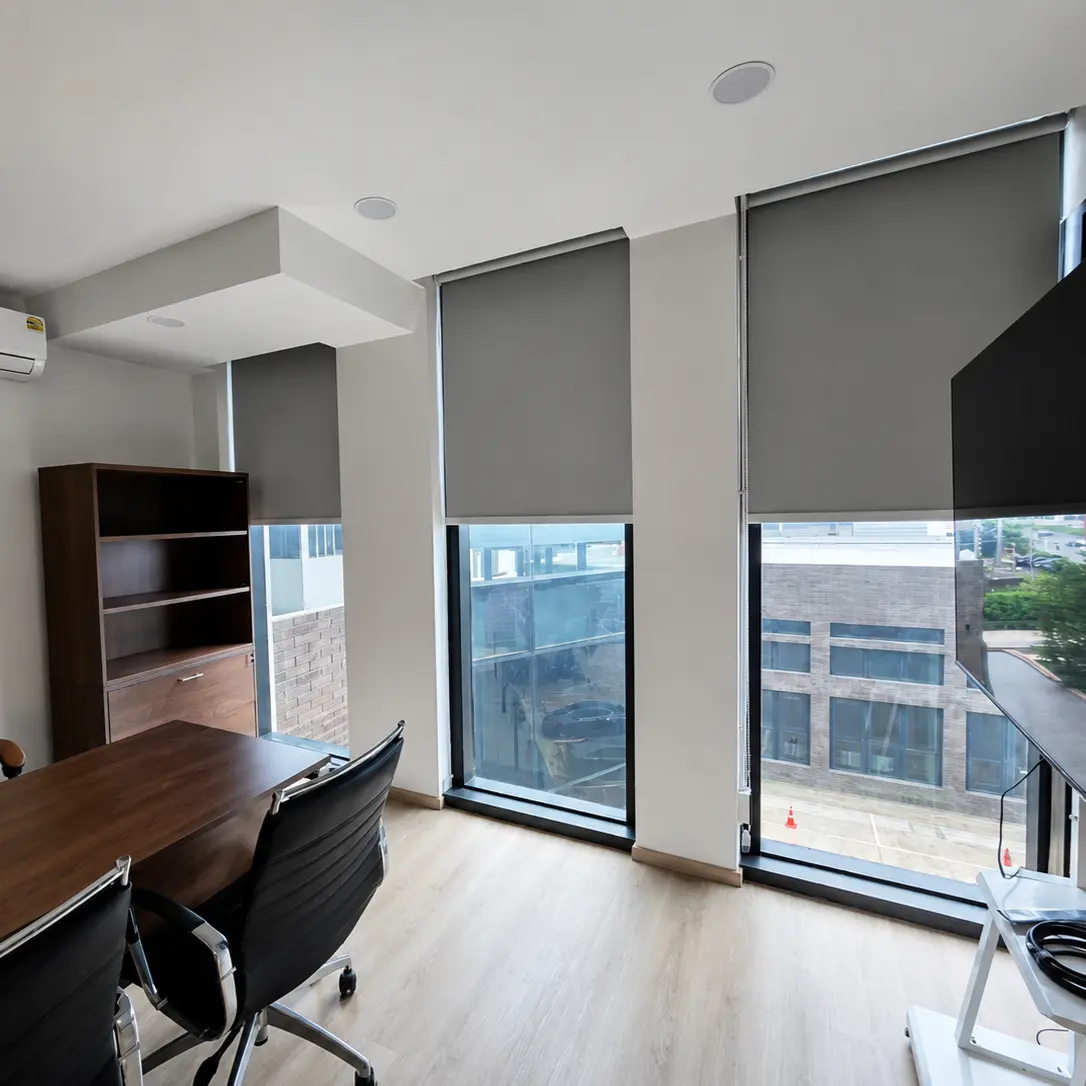 Executive office with gray roller blinds on floor-to-ceiling windows, leather chair and wood desk