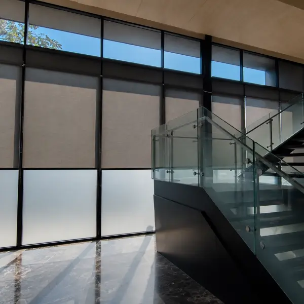 Stairwell atrium with tall taupe roller blinds along floor-to-ceiling windows and glass railings