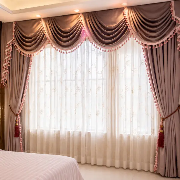 Bedroom with a mauve swag-and-tail valance, tassel trim, and tieback curtains beside an arched gold-lit mirror alcove