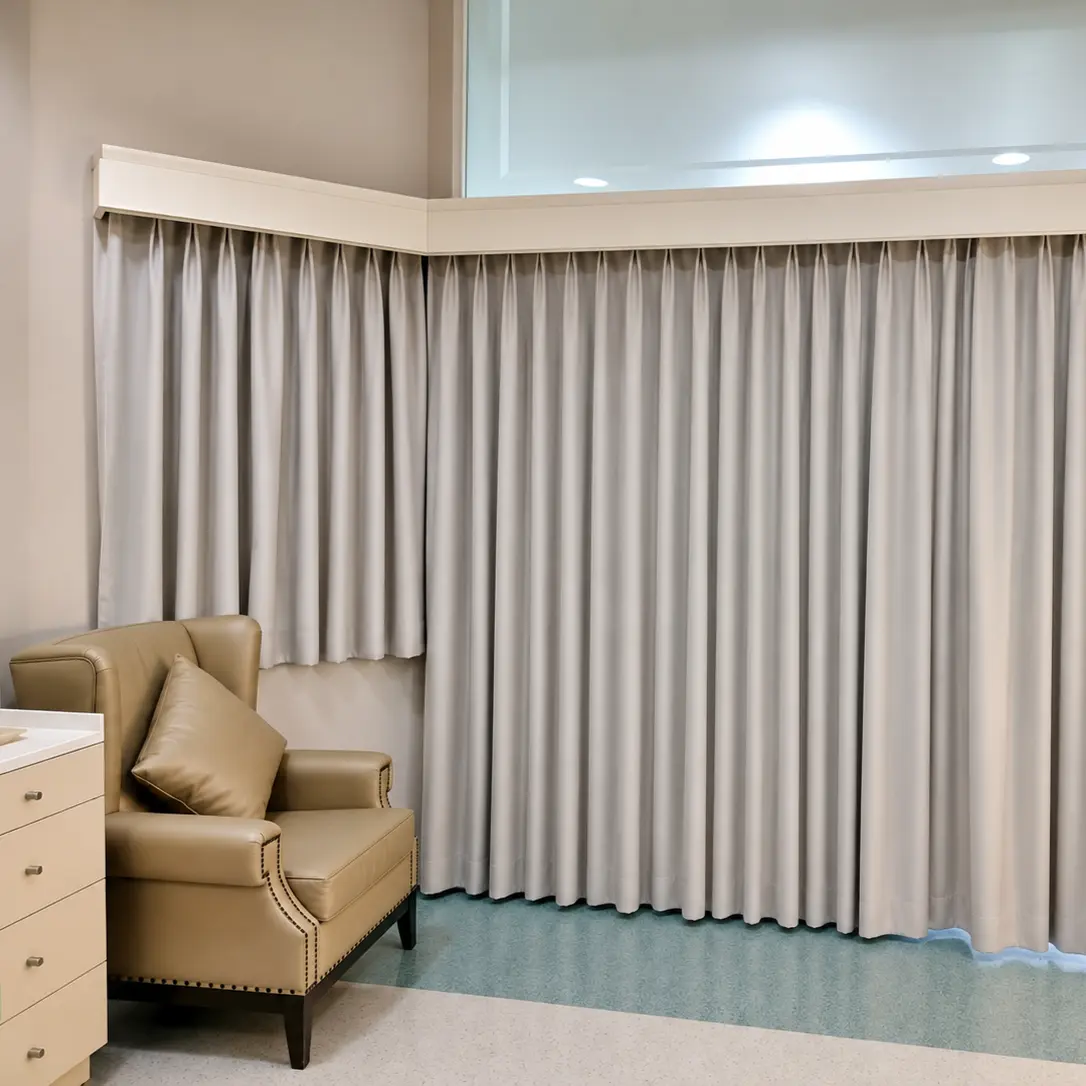 Hospital room with pleated privacy curtain track along the wall, beside a leather armchair