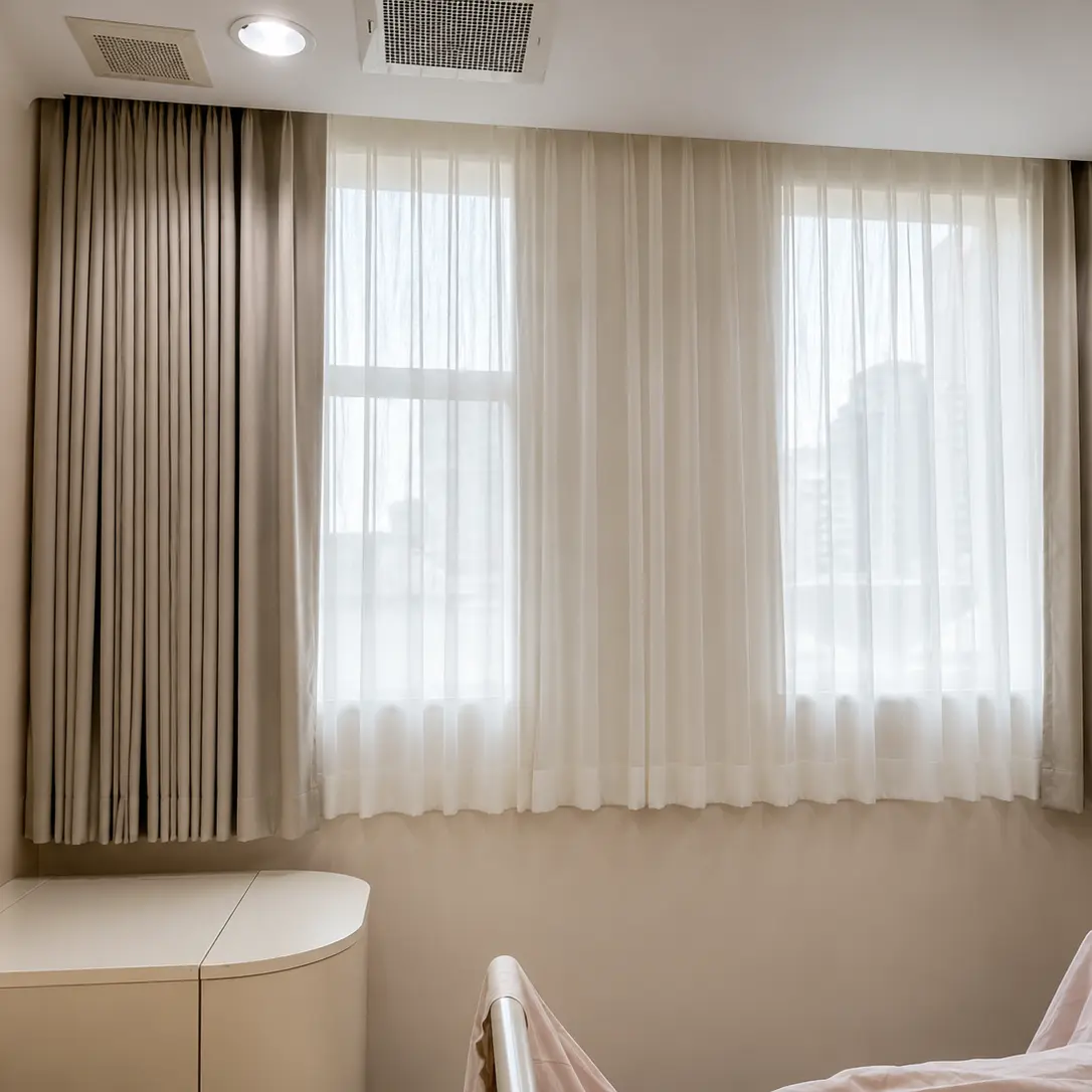 Sheer and blackout curtain layers on a hospital room window beside a medical monitor stand