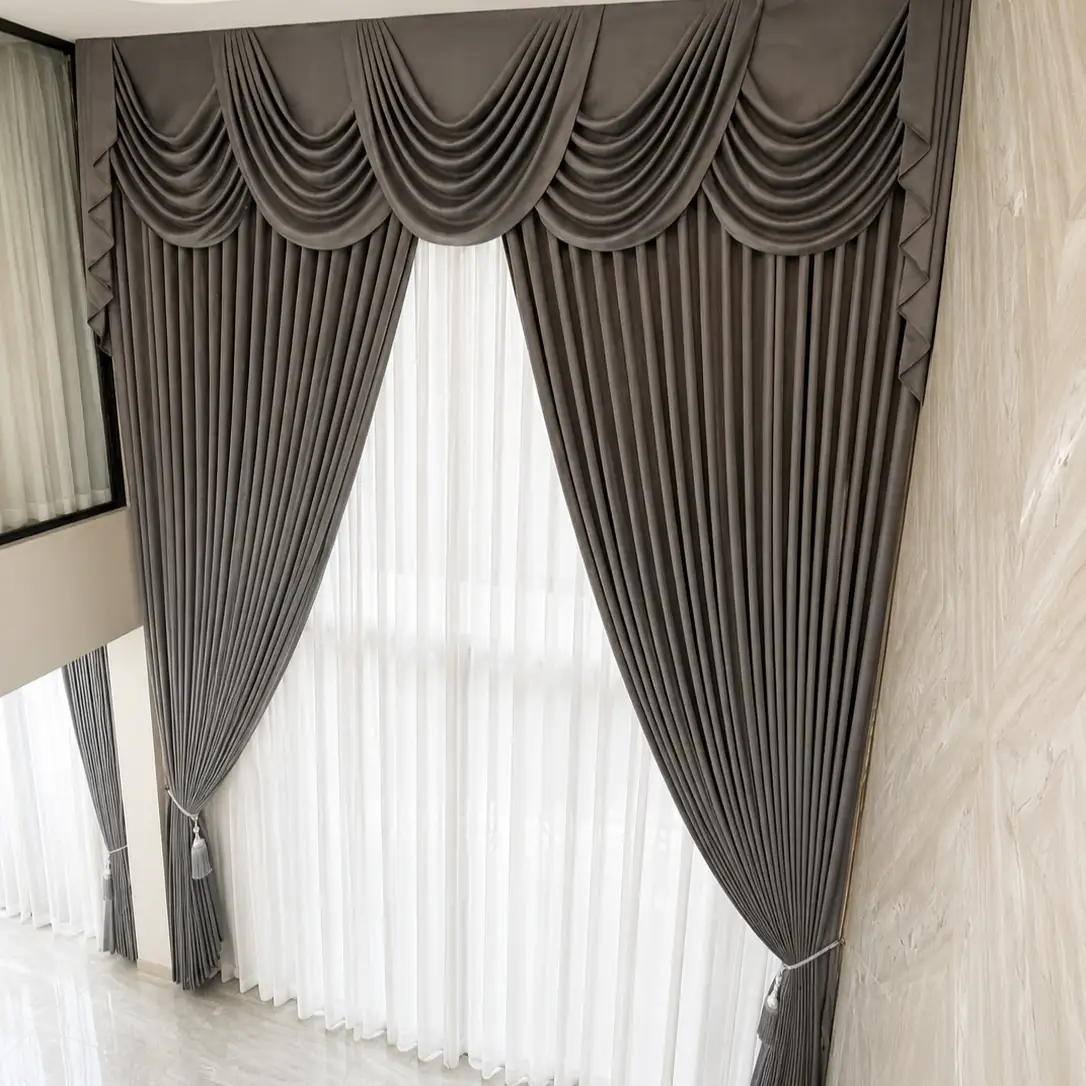 Tall double-height window with a taupe swag valance curtain against a marble wall, reflection of another curtain visible alongside