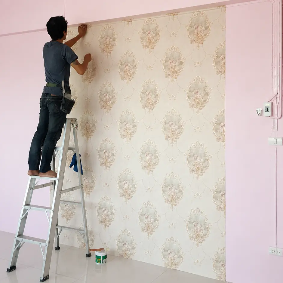 Technician on a ladder installing cream floral damask wallpaper in a room with pink walls
