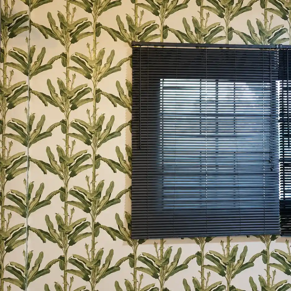 Green banana leaf pattern wallpaper on a wall beside black venetian blinds