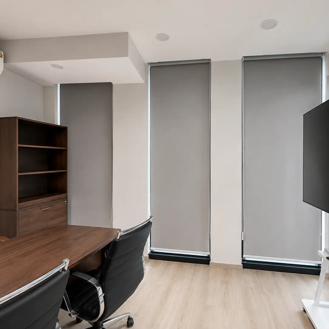 Executive office with three gray roller blinds fully lowered over floor-to-ceiling windows, wood bookshelf and wall-mounted TV