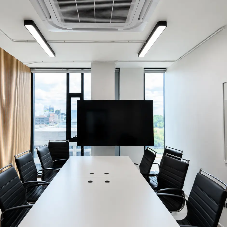 Meeting room with a long conference table, black leather chairs, and floor-to-ceiling windows with blinds raised, wood slat accent wall and wall-mounted TV