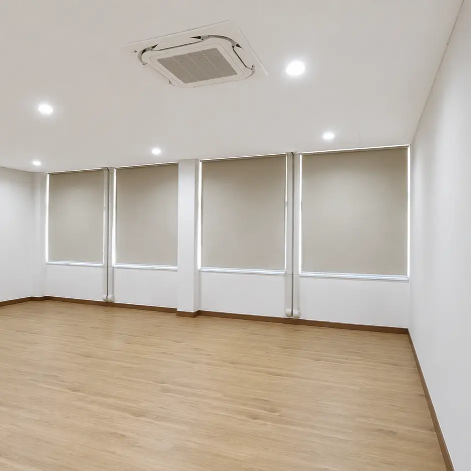 Empty office room with wood flooring and four roller blinds covering floor-to-ceiling windows
