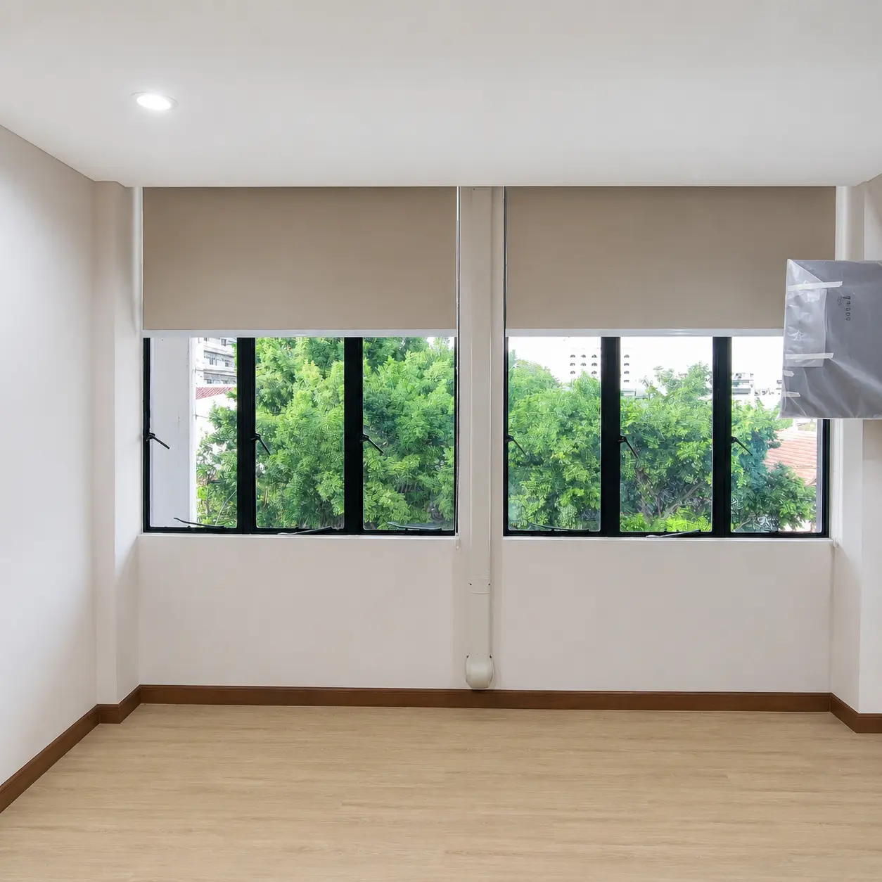 Two windows with roller blinds partially raised, revealing a view of trees outside