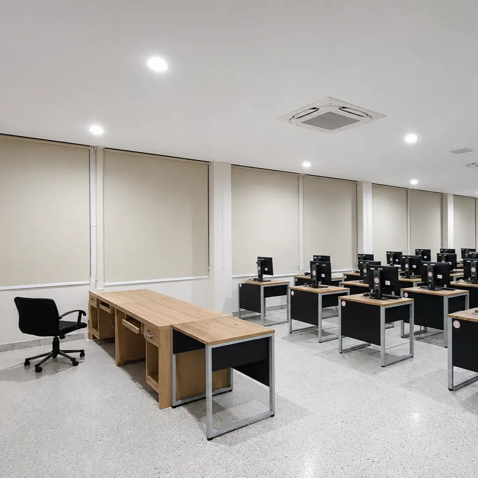 Computer training room with rows of desktop monitors and roller blinds along the side windows