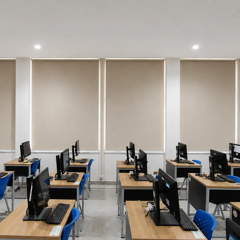 Computer training room viewed from the front, rows of desks with monitors and closed roller blinds behind