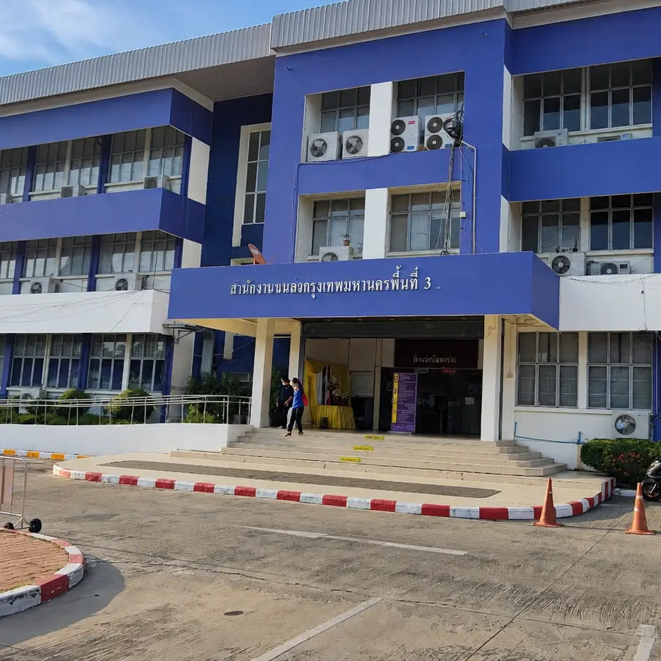 Exterior of a three-story blue and white government office building with a Bangkok Metropolitan Land Transport Office sign, motorcycles parked out front