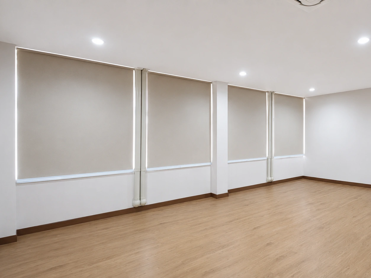 Empty office room with wood flooring and four roller blinds covering floor-to-ceiling windows