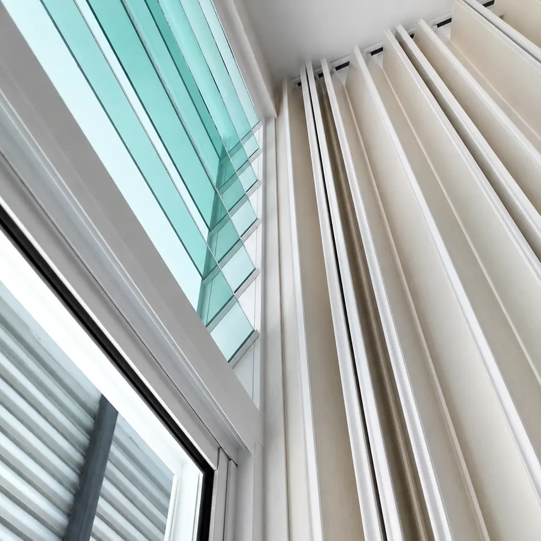 Close-up of pleated curtain fabric on a ceiling track beside glass louver windows